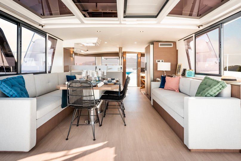 Bali 4.6 kiralık katamaranın salonu, üç tarafında panoramik camlar ve uzun bir yemek kanepesiyle donatılmıştır.
