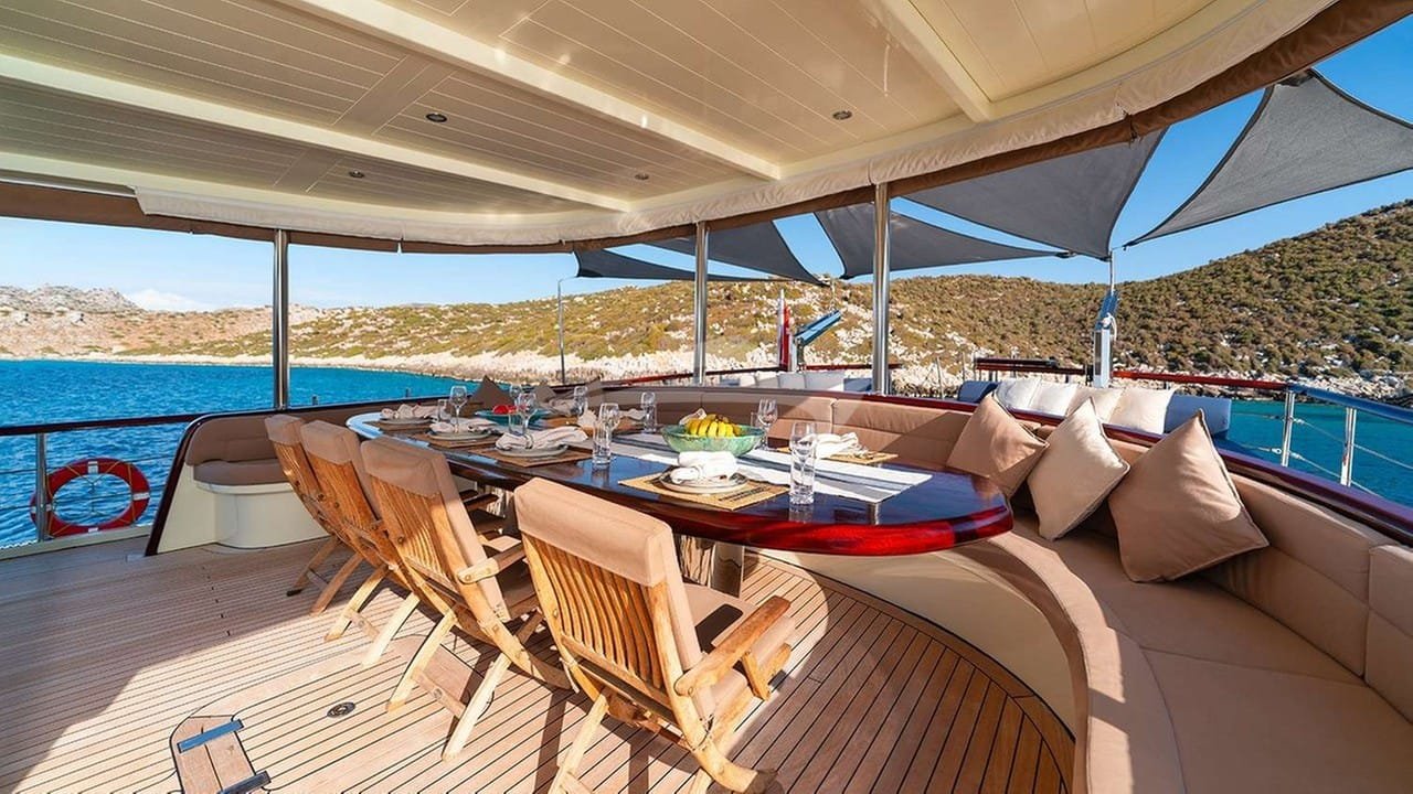 Aft deck dining table of a crewed motor yacht charter in Gocek laid for twelve under sun shades