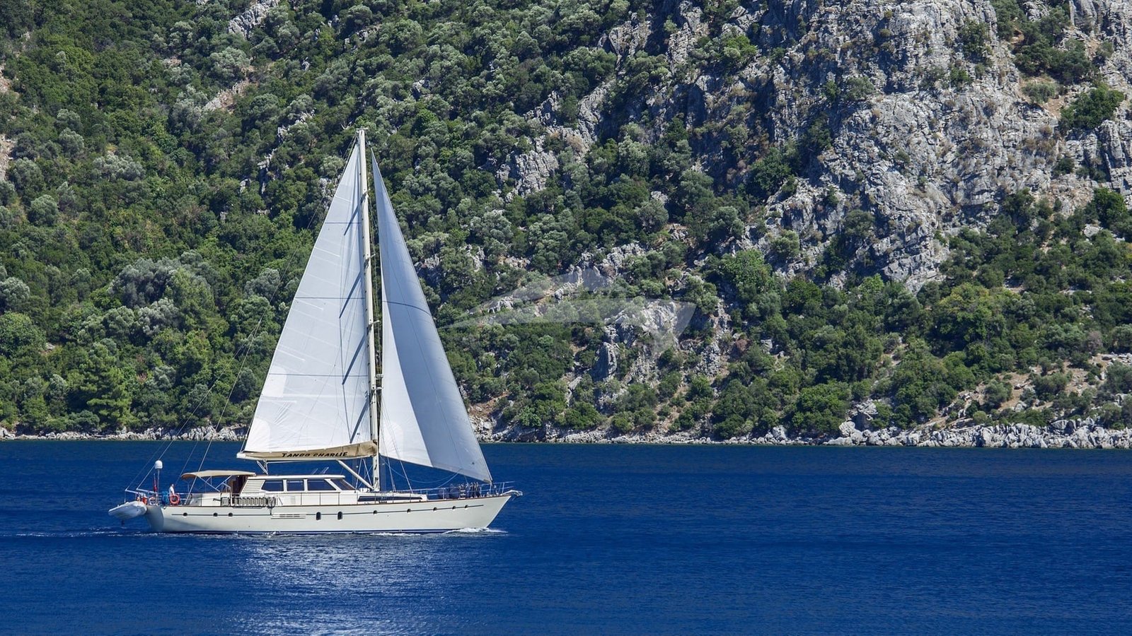 Crewed sailing yacht charter from Bodrum - 26m sloop under sail beneath a limestone headland