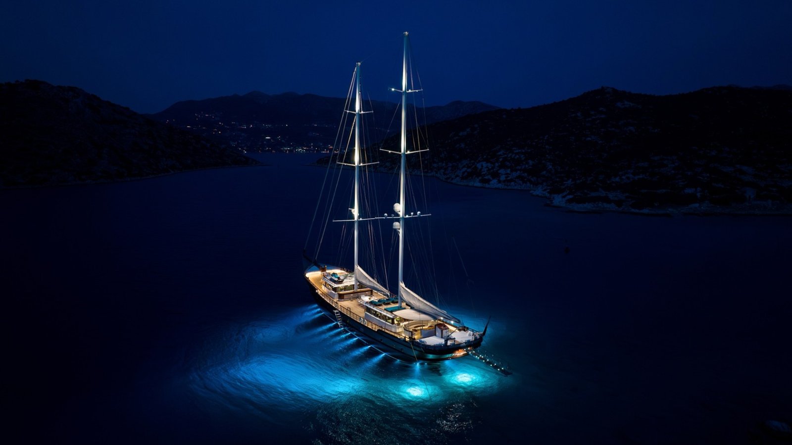 Aerial night view of a 43m motor sailer with underwater lights at anchor — MN4308