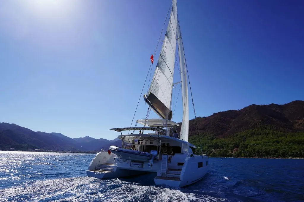 Lagoon 46 catamaran charter Marmaris under sail off a Turkish headland with the flag streaming aft
