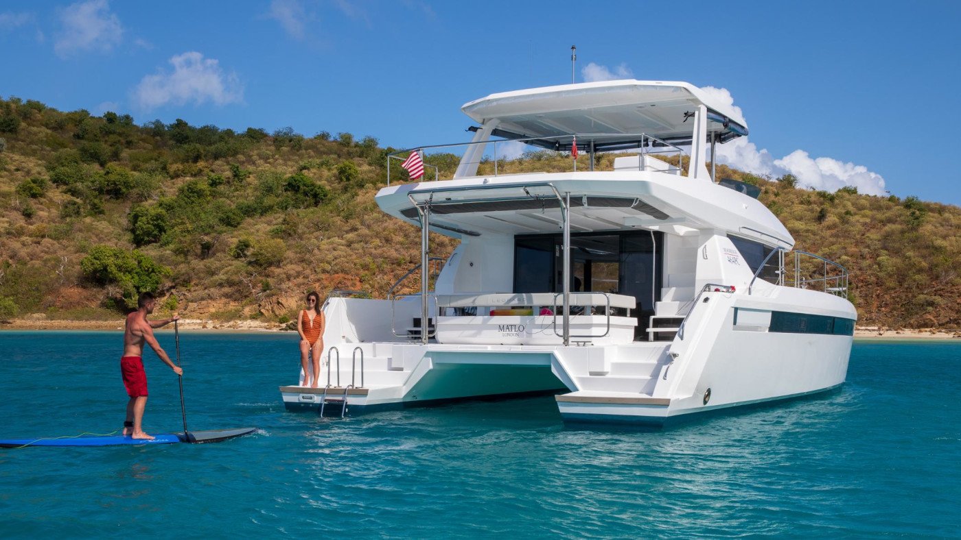 Guests paddleboarding beside the wide swim platform of a Leopard 46 Powercat charter catamaran in a sheltered Turkish bay