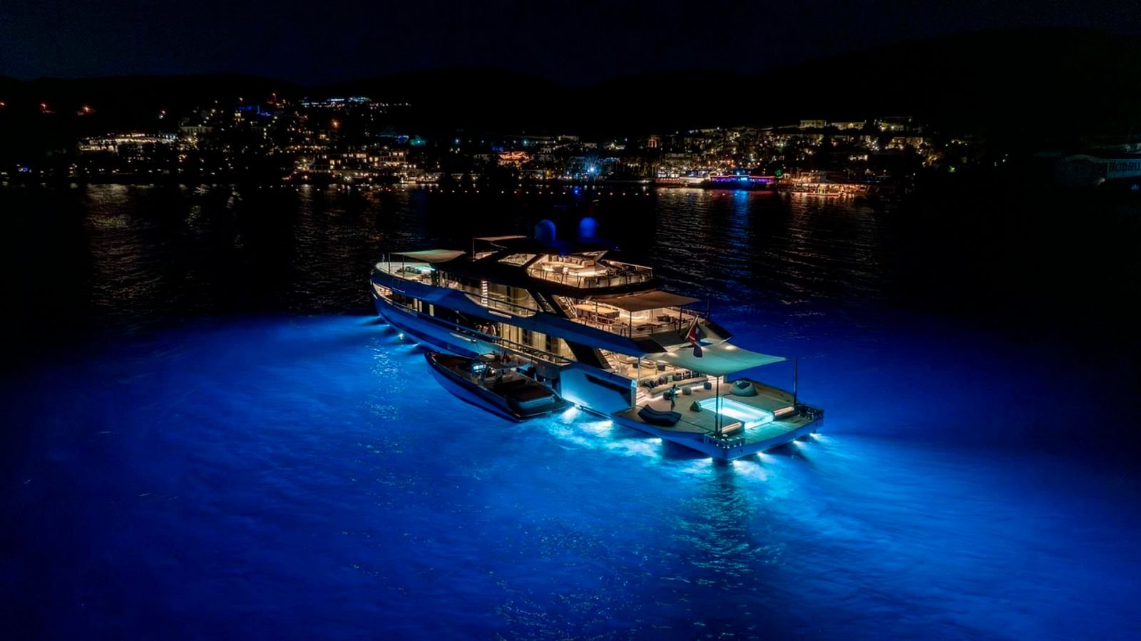 A 50m mega yacht lit at night off Bodrum, seen from the air