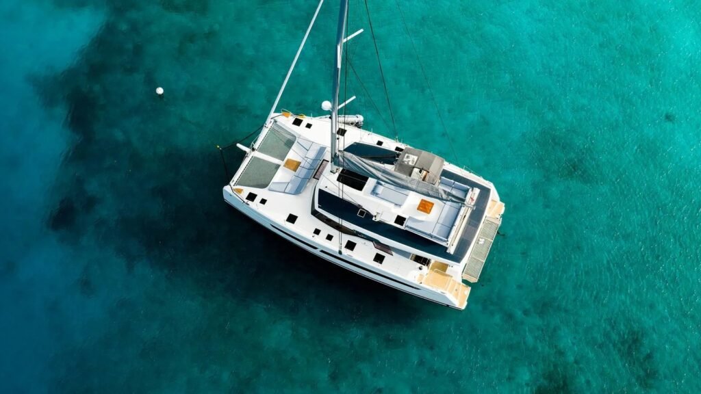 Aura 51 catamaran aerial view anchored in a sheltered sandy bay with tender alongside, Rhodes charter AM1604