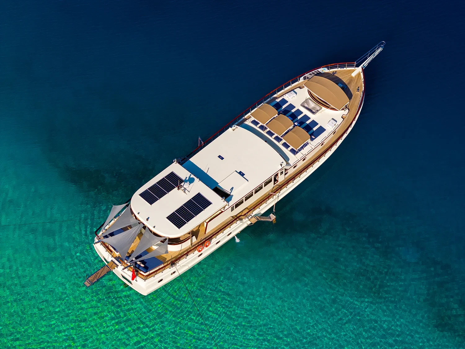 Drone view at an angle onto the sundeck of a crewed motor yacht charter in Gocek, sun loungers and awnings visible