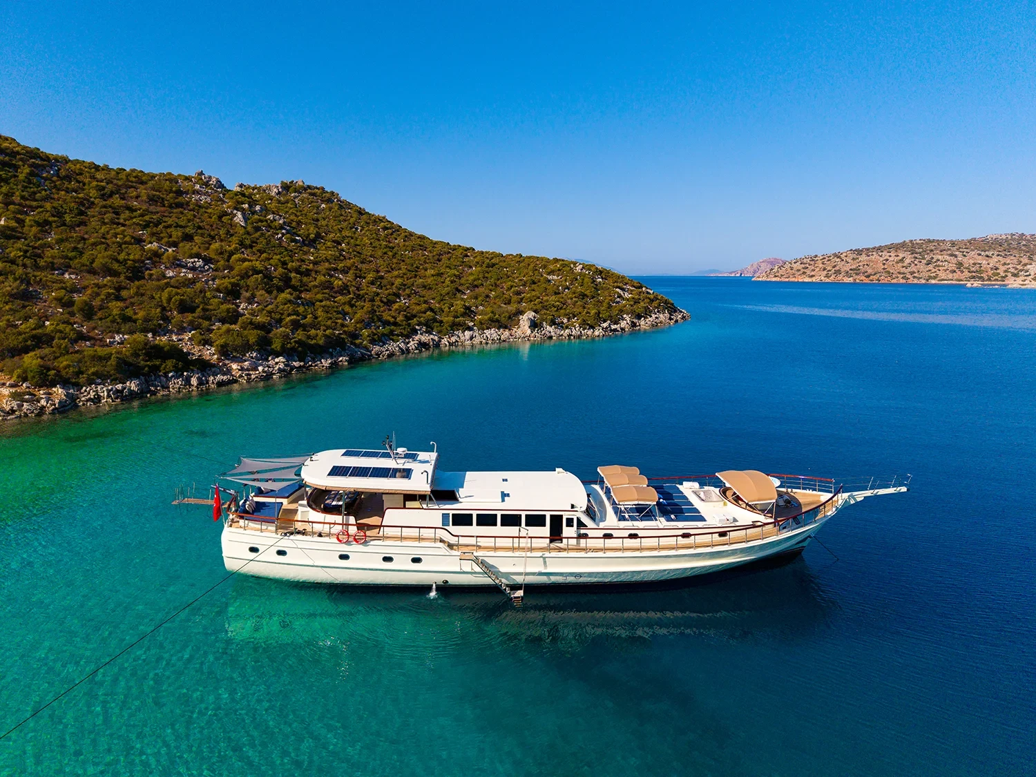 Aerial view of a crewed motor yacht charter in Gocek anchored in a turquoise cove surrounded by pine hills