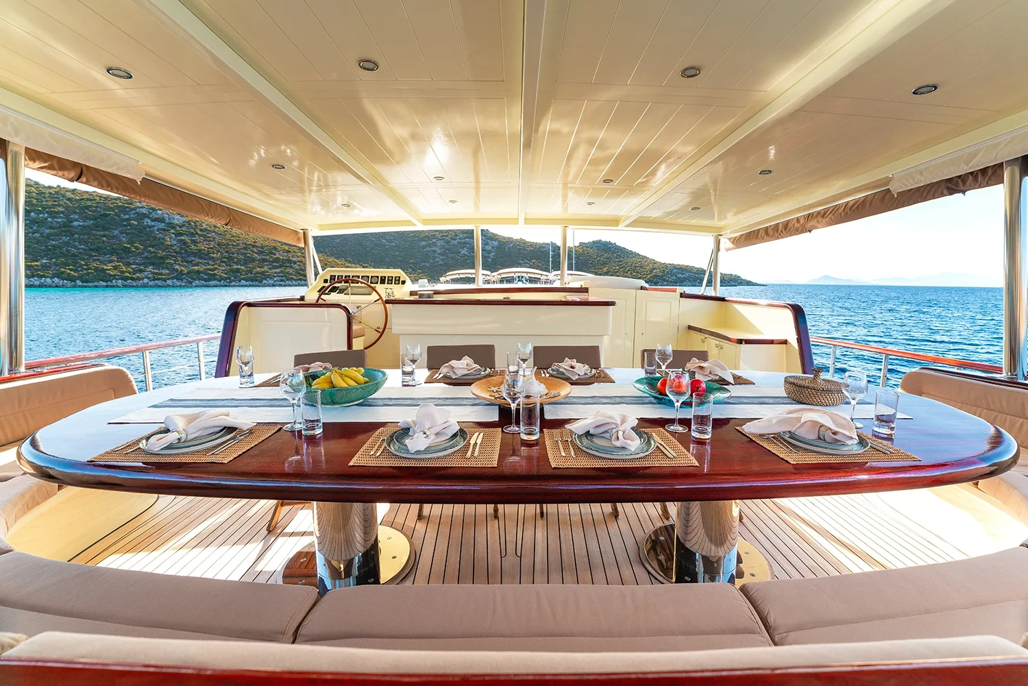 Aft dining and seating area aboard a crewed motor yacht charter in Gocek, table set for eight beside the upper helm