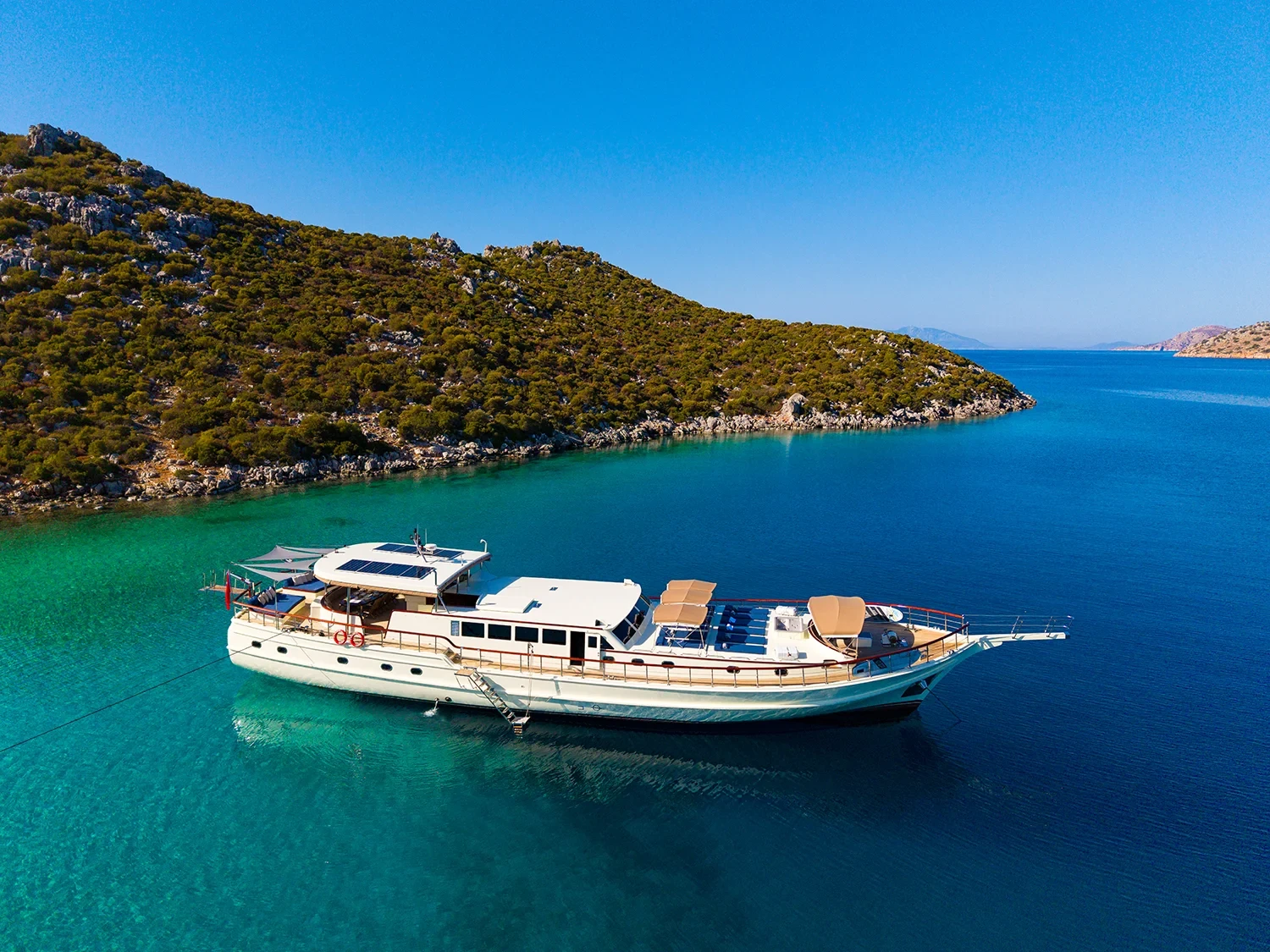 Crewed motor yacht charter Gocek at anchor in a turquoise cove, classic profile with red-trimmed hull
