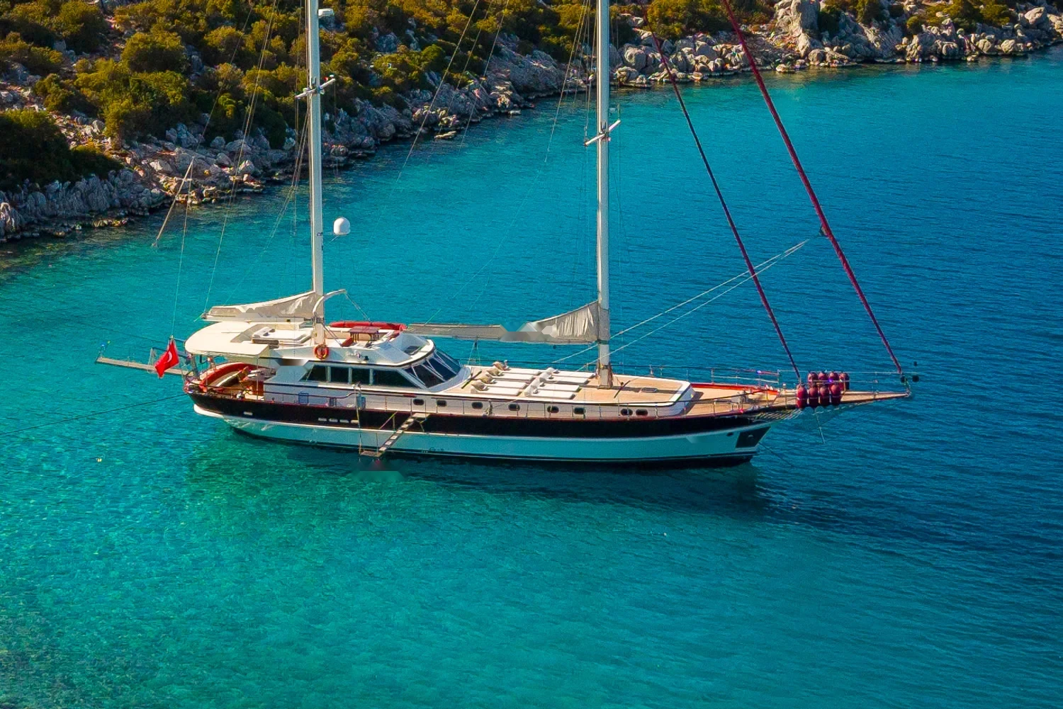 Deluxe motor sailer charter Gocek at anchor in a turquoise cove with sails furled