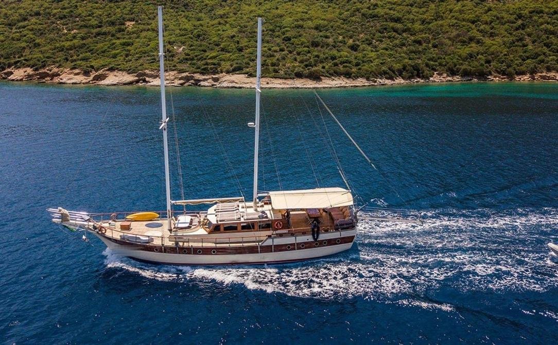 Bodrum samimi gulet kiralama - kayalık bir kıyı açıklarında seyreden 24m guletin havadan görünümü