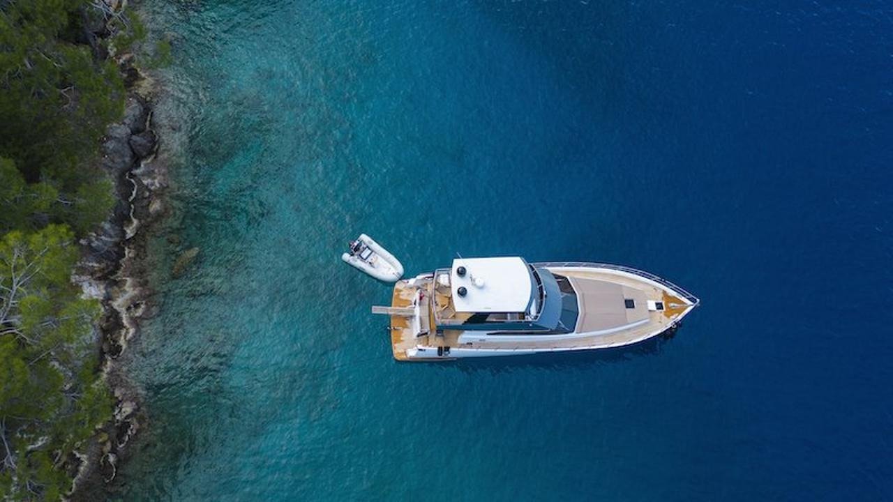 Aerial drone view of a luxury motor yacht anchored in a turquoise Fethiye cove with tender alongside