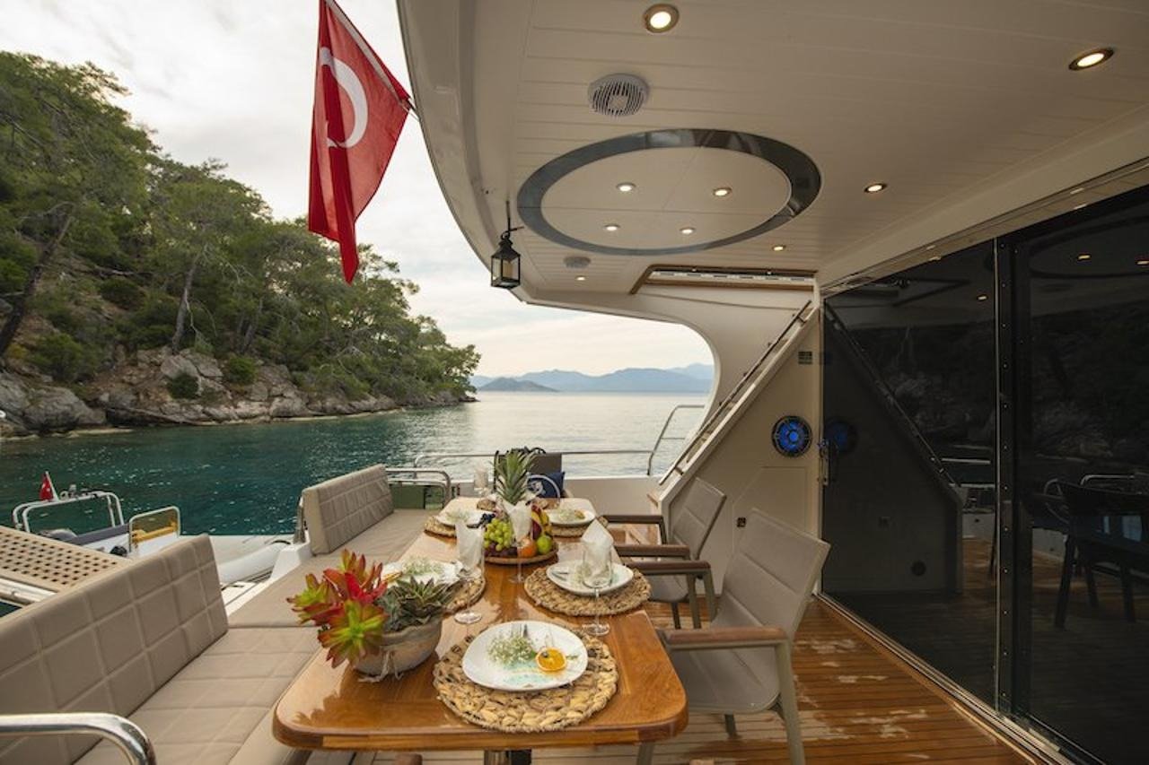 Cockpit dining table with fruit and place settings aboard a luxury motor yacht overlooking a rocky Fethiye cove
