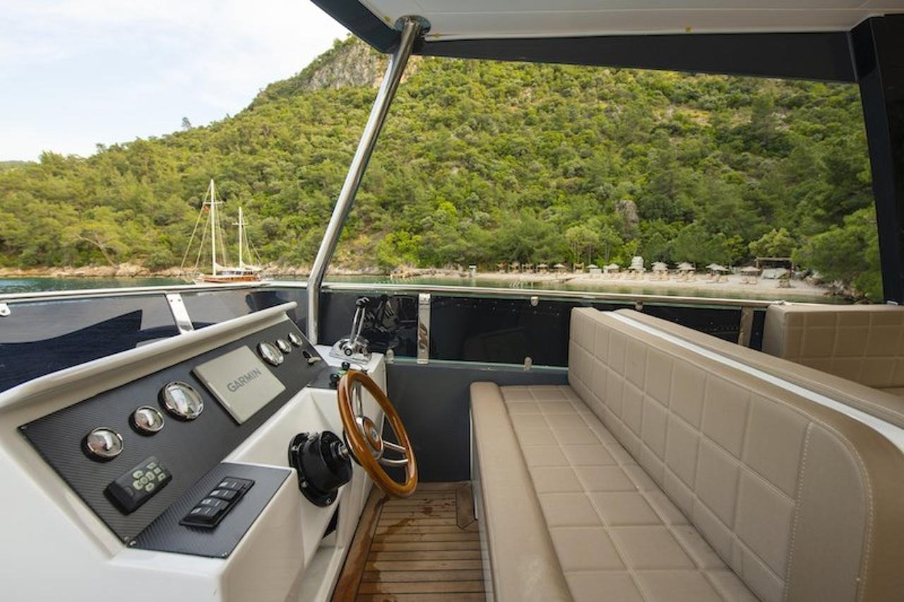 Upper flybridge helm station and guest seating on a luxury motor yacht overlooking a Fethiye beach cove