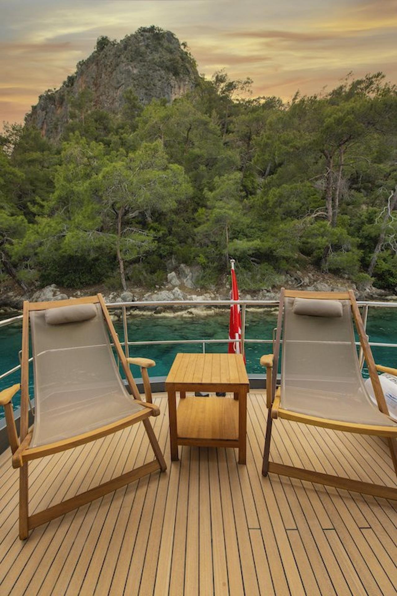 Teak sun loungers on the flybridge of a luxury motor yacht facing a pine-covered Fethiye headland