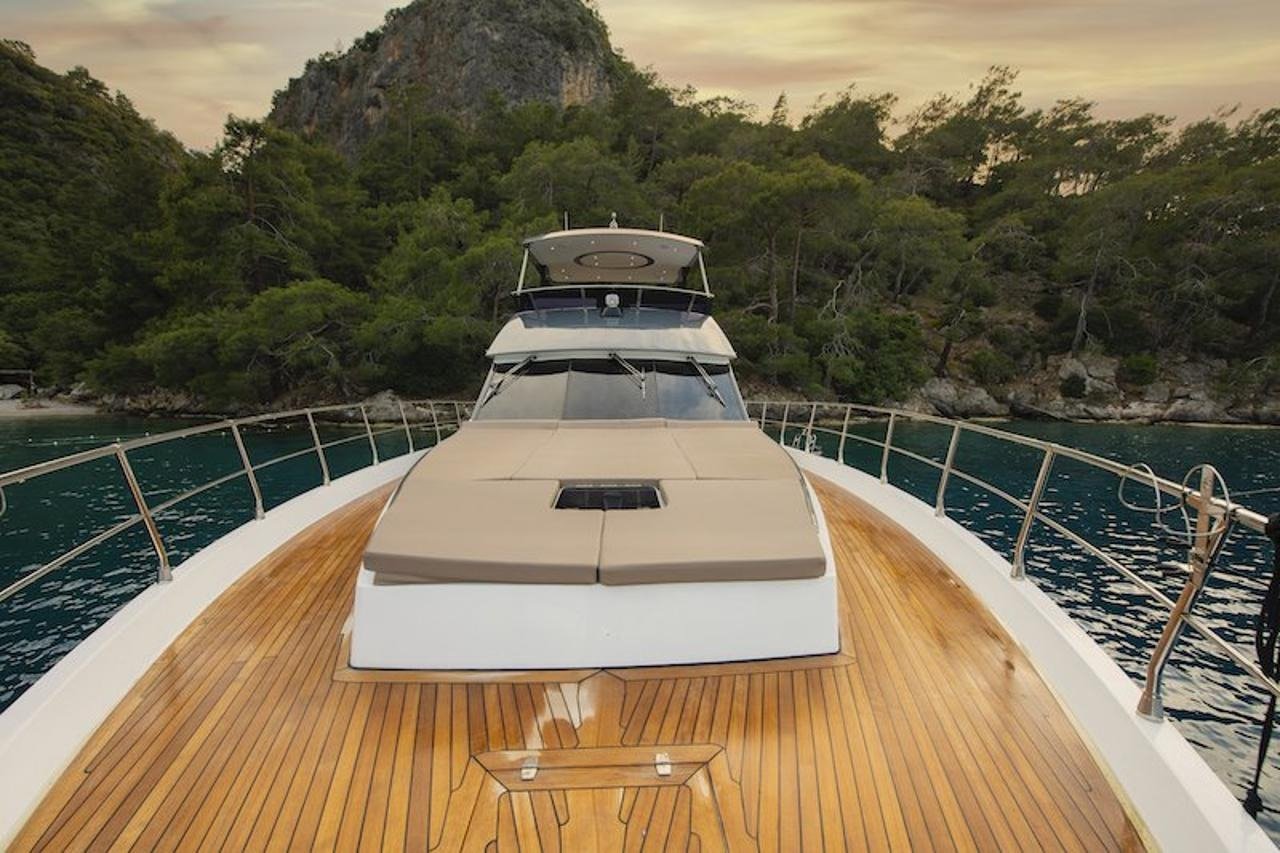 Teak foredeck with sunpads on a luxury motor yacht overlooking a wooded Fethiye bay