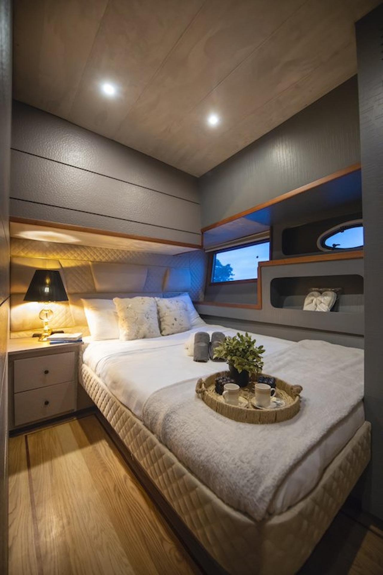 Master cabin with a plush double bed and turned-down linens aboard a luxury motor yacht at dusk