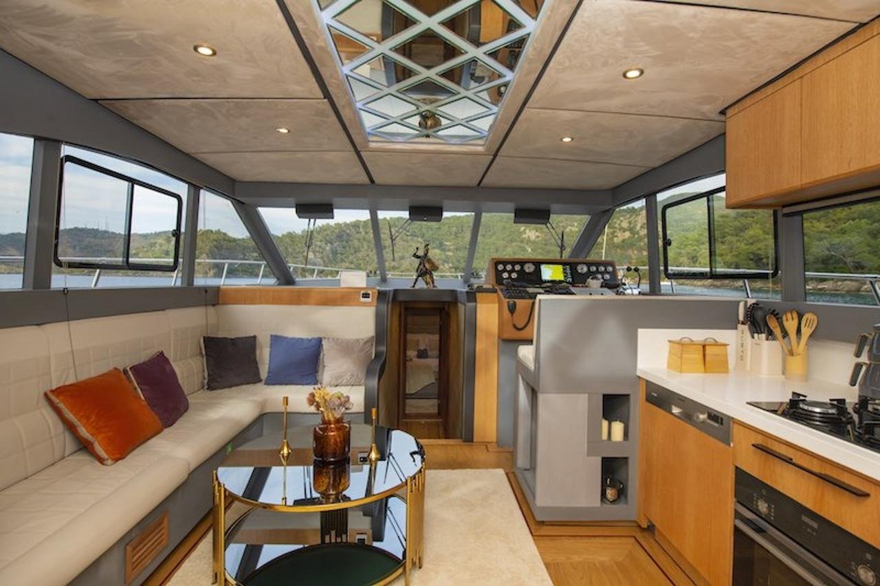 Main saloon lounge and helm station aboard a luxury motor yacht with panoramic windows over a Fethiye anchorage