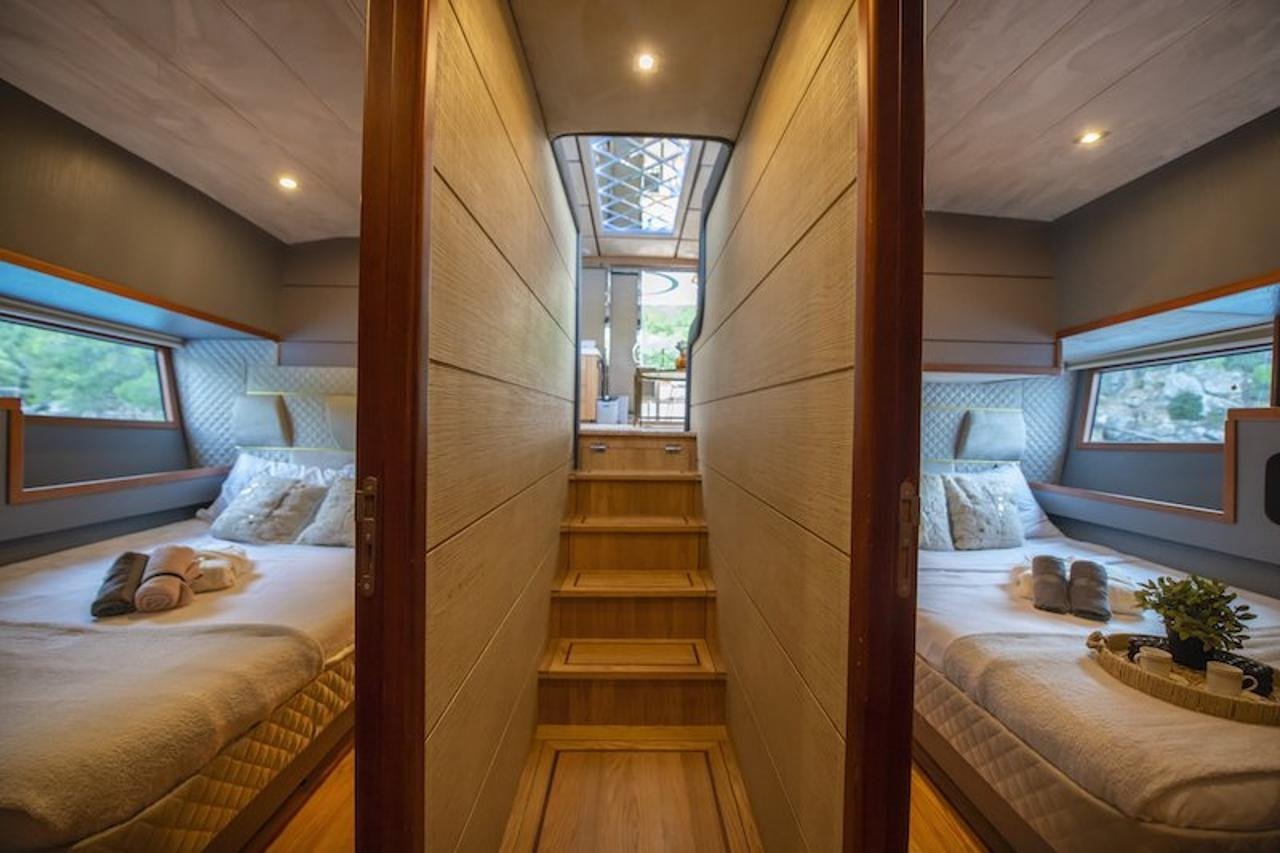 Mirrored twin guest cabins with quilted headboards aboard a luxury motor yacht, connected by a central companionway