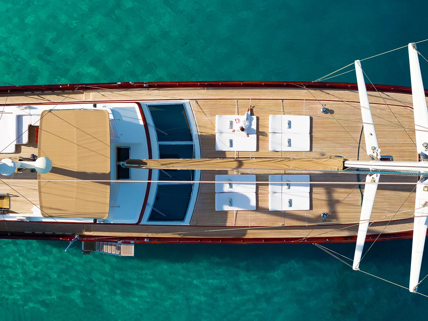 Bird's eye drone view of a sailing yacht charter Bodrum bow sundeck, guest relaxing on white loungers