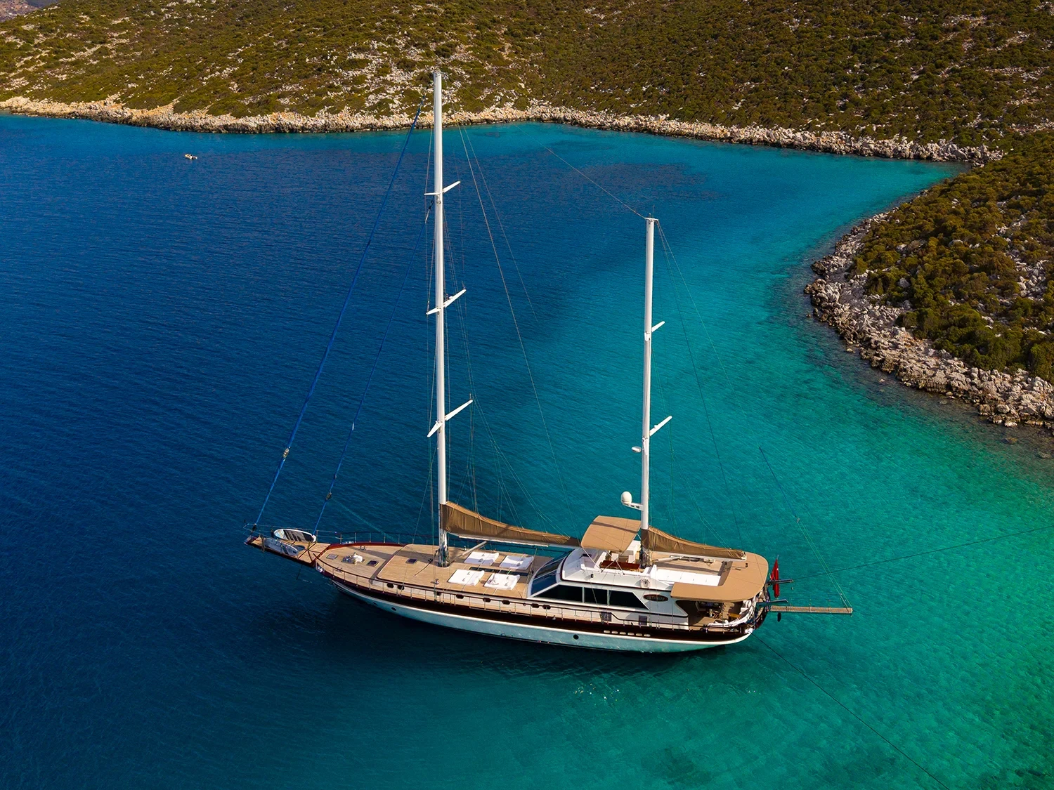 Aerial view of a sailing yacht charter Bodrum anchored in a secluded turquoise cove surrounded by pine hills