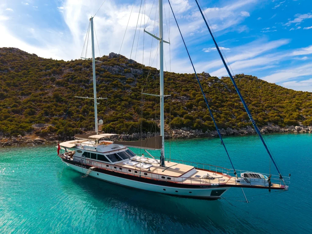 Sailing yacht charter Bodrum photographed from a drone at anchor in a turquoise cove, full side profile with both masts