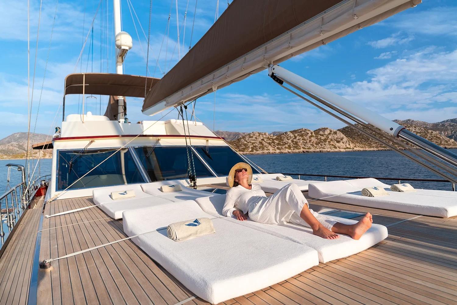 Guest relaxing on foredeck sun mattresses of a sailing yacht charter in Bodrum with mountains behind