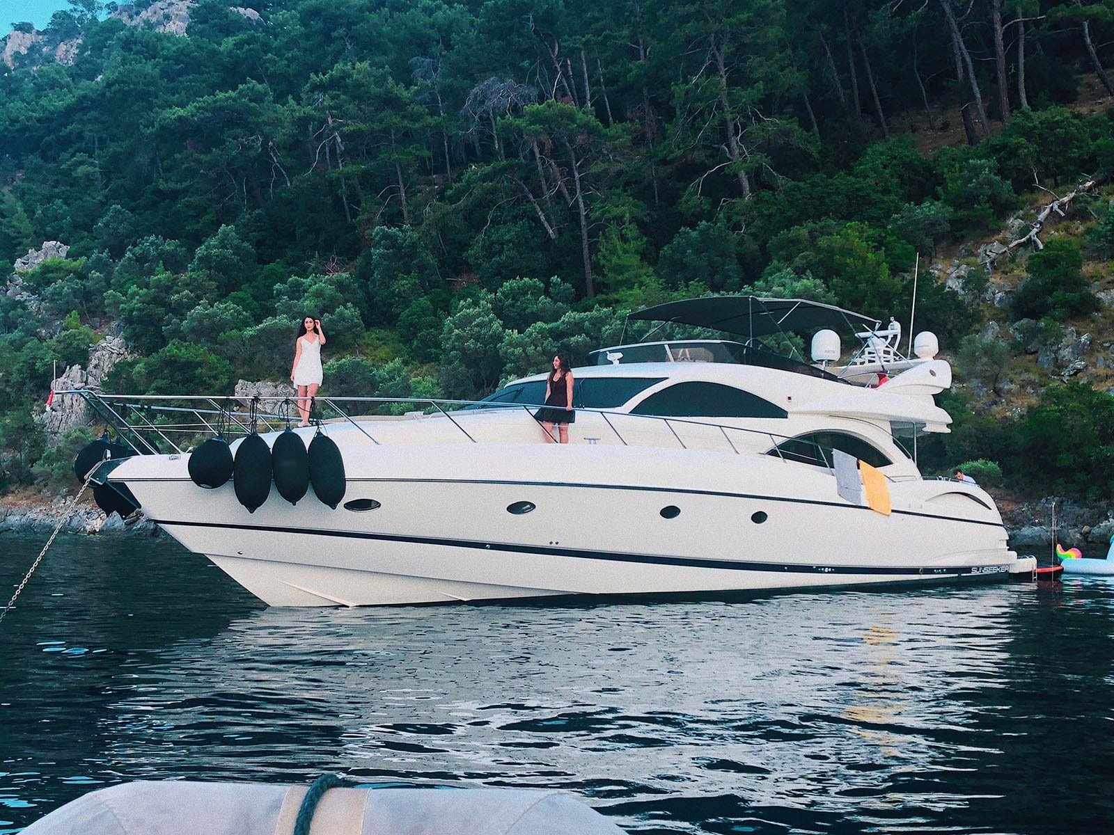 Guests aboard a Sunseeker Manhattan 74 charter yacht anchored beneath a pine-covered shoreline near Göcek