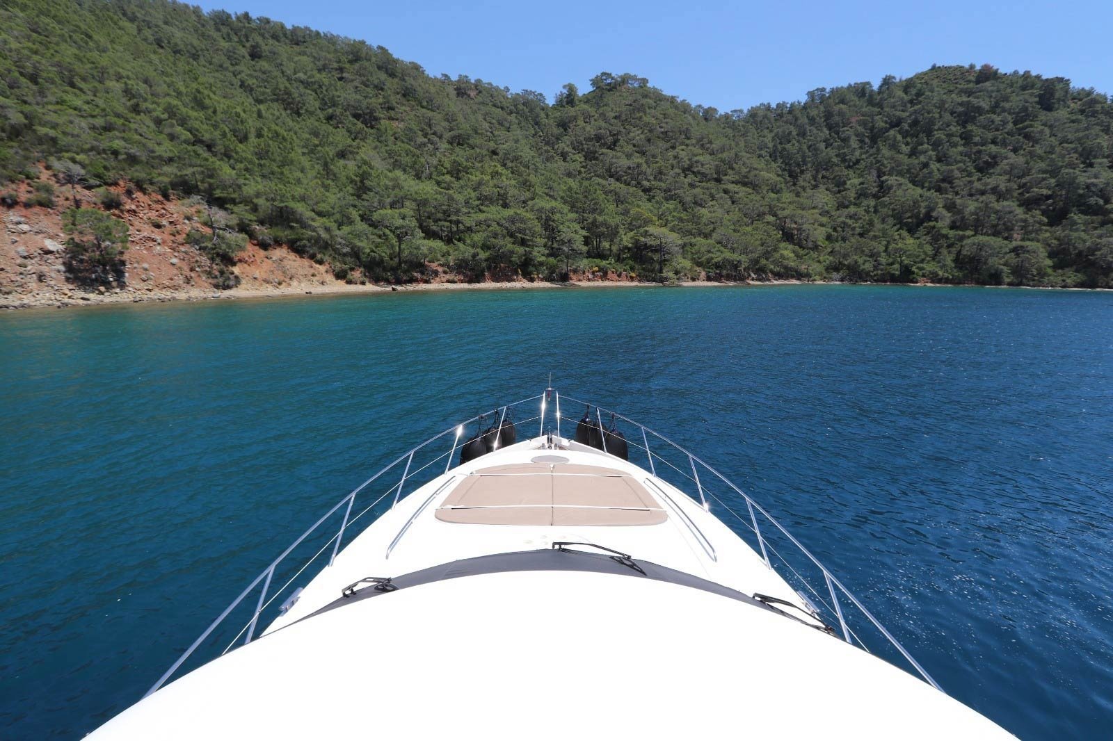 View forward over the foredeck and pulpit of a Sunseeker Manhattan 74 towards a pine-clad Göcek bay
