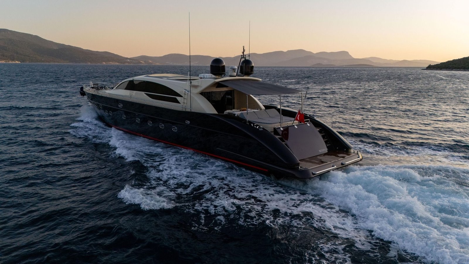 Tecnomar 116 charter Bodrum cruising at sunset with her navy hull catching the light
