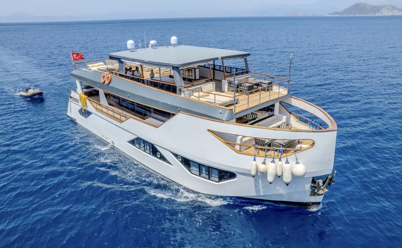 Aerial bow view of a trawler charter Fethiye anchored in a pine-fringed Turkish cove