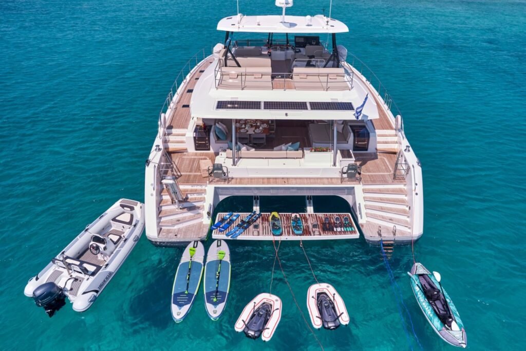 Fountaine Pajot Power 67 charter catamaran at anchor in the Cyclades, aerial stern view with water toys laid out
