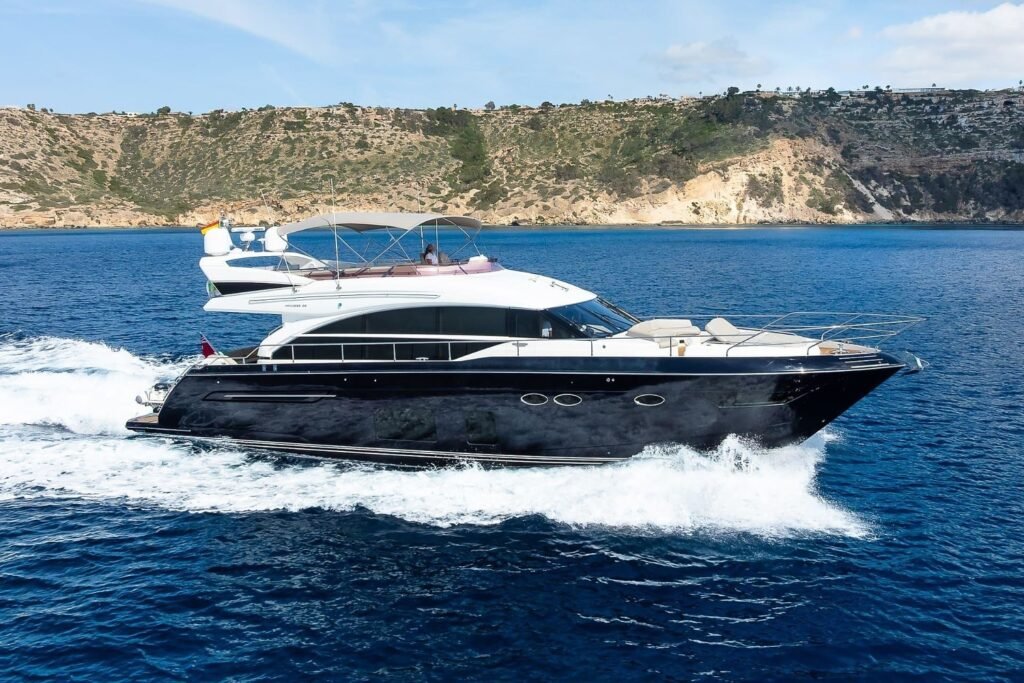 Princess 68 flybridge motor yacht with navy blue hull cruising along a Mediterranean coastline on a luxury crewed charter